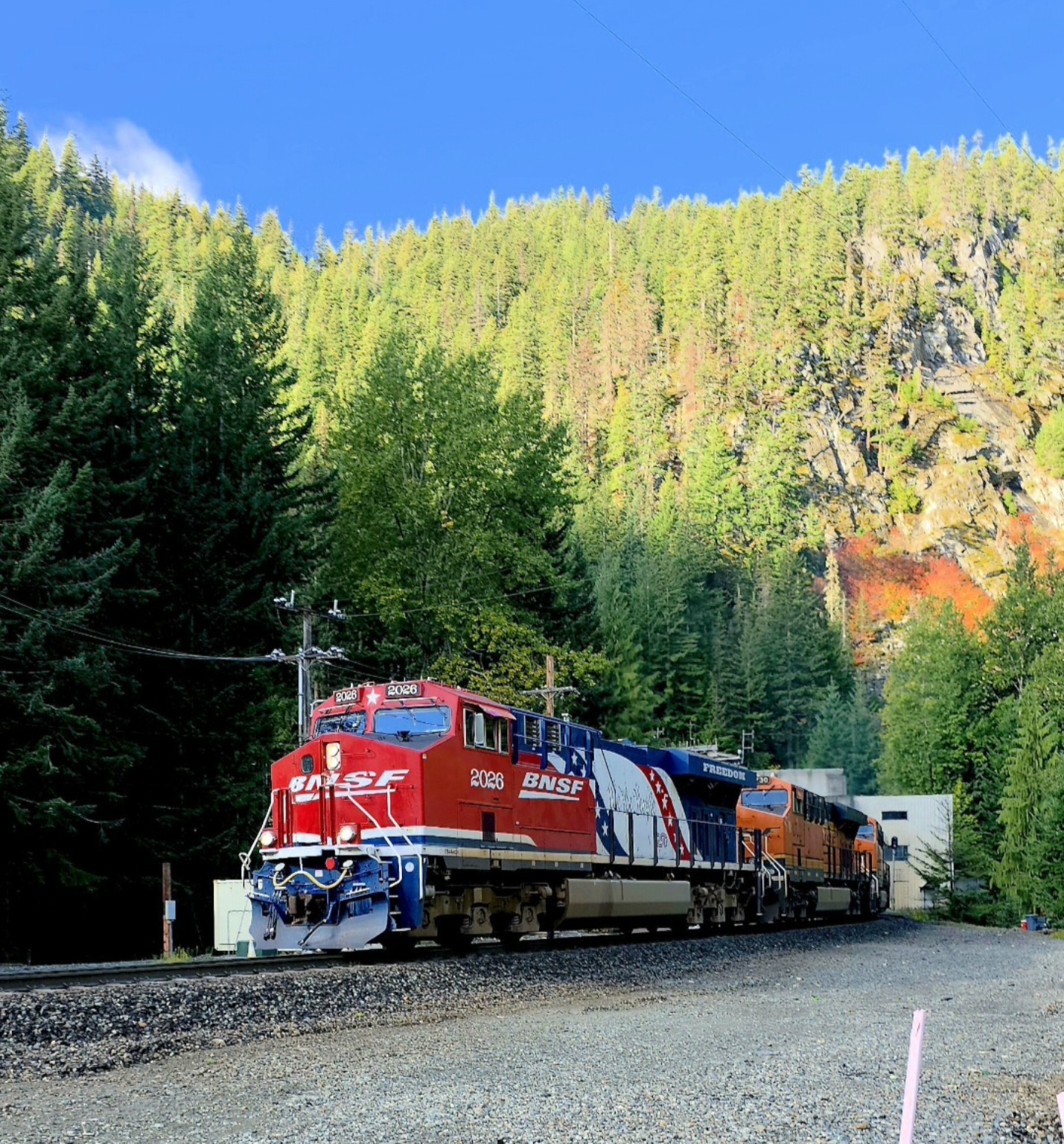 BNSF 2026 rounding a curve beneath a forested rock face with autumn color